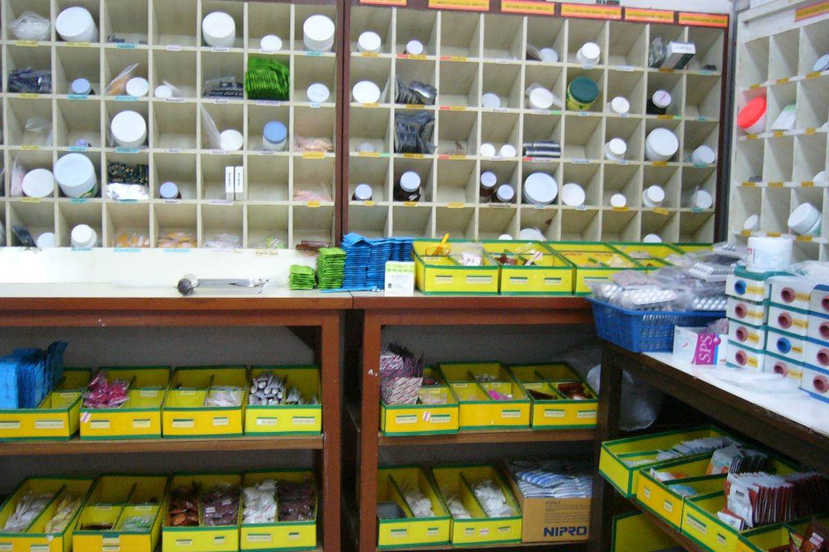 A hospital pharmacy: medicine jars in labelled pigeonholes over trays of tablets.